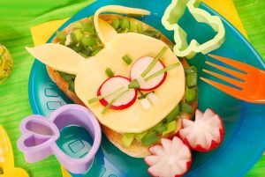 Na obrazku widoczna kanapka obłożona sałatą i żółtym serem. dekorację tworzy rzodkiewka i szczypiorek tworząc postać królika